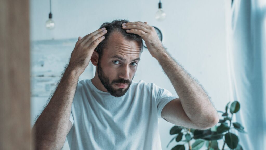 Man looking in the mirror at his receding hairline form of hair loss