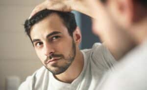 Close-up of a man gently touching his scalp with visible thinning hair, illustrating the first signs of hair loss and the need for early intervention.